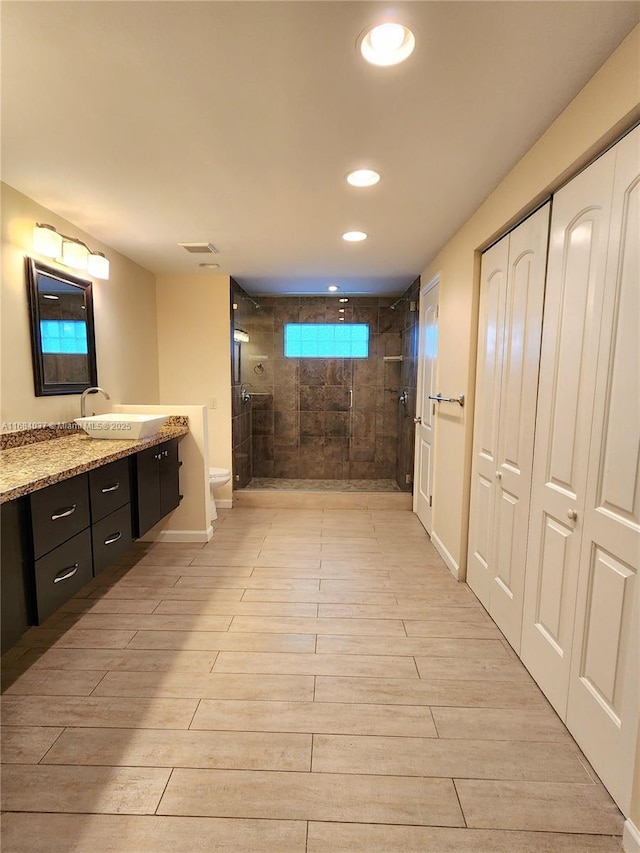 bathroom with tiled shower, vanity, hardwood / wood-style flooring, and toilet