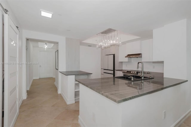 kitchen with sink, a barn door, kitchen peninsula, hanging light fixtures, and white cabinets