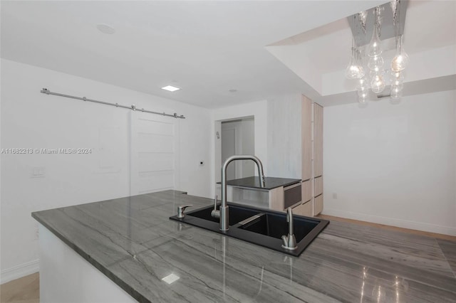 kitchen with a barn door, wood-type flooring, sink, a notable chandelier, and decorative light fixtures