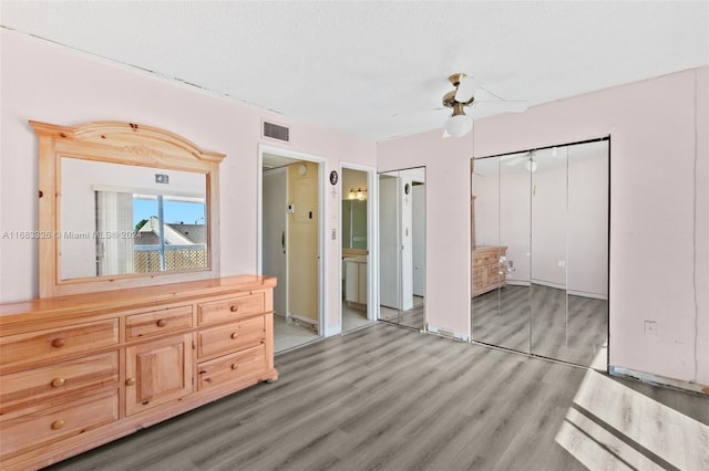 unfurnished bedroom featuring a textured ceiling, two closets, wood-type flooring, and ceiling fan