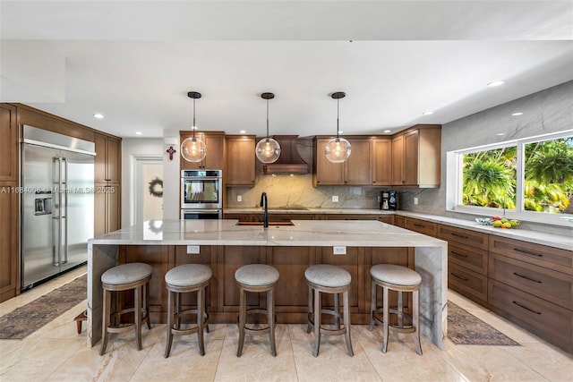 kitchen with hanging light fixtures, appliances with stainless steel finishes, a kitchen island with sink, and backsplash