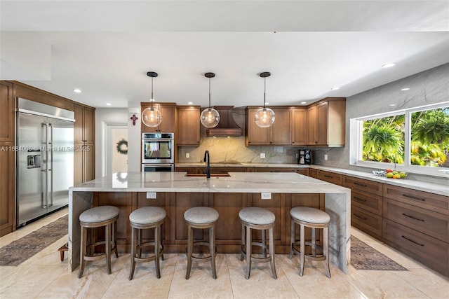 kitchen with premium range hood, stainless steel appliances, decorative light fixtures, tasteful backsplash, and a spacious island