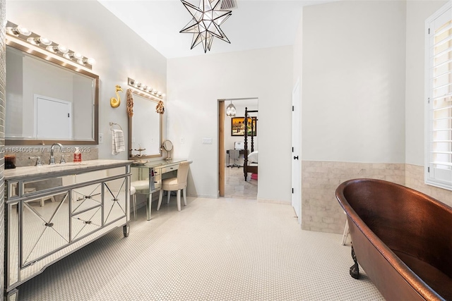 bathroom with a freestanding bath, wainscoting, vanity, a chandelier, and tile walls