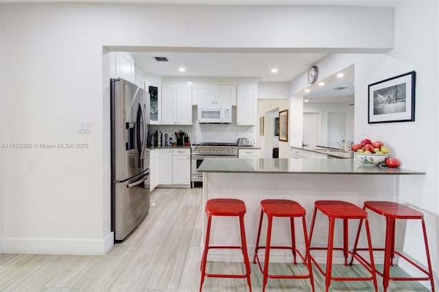 kitchen featuring stainless steel appliances, tasteful backsplash, white cabinets, a kitchen bar, and kitchen peninsula