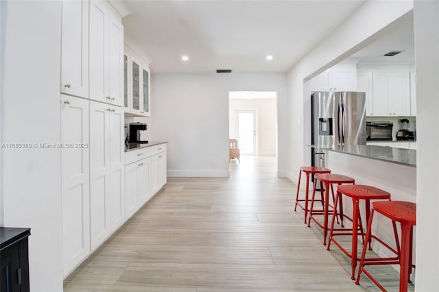 kitchen with white cabinetry, light hardwood / wood-style floors, a breakfast bar, and stainless steel refrigerator with ice dispenser