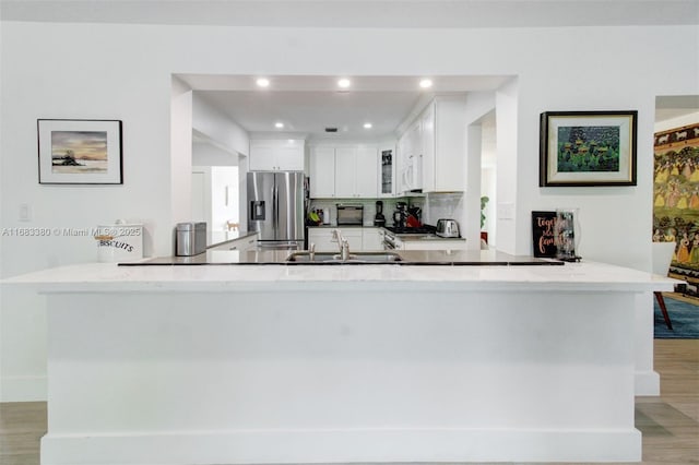 kitchen featuring sink, stainless steel refrigerator with ice dispenser, light hardwood / wood-style floors, white cabinets, and kitchen peninsula