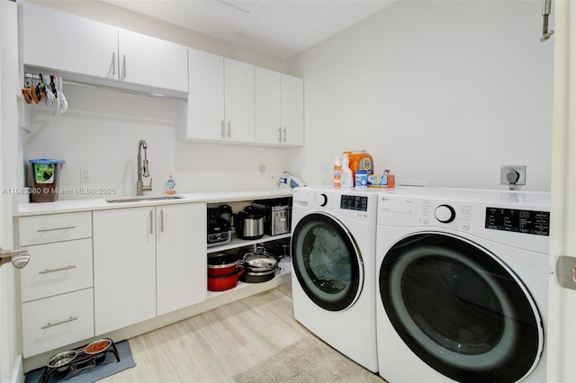 clothes washing area featuring sink, light hardwood / wood-style floors, cabinets, and washing machine and clothes dryer