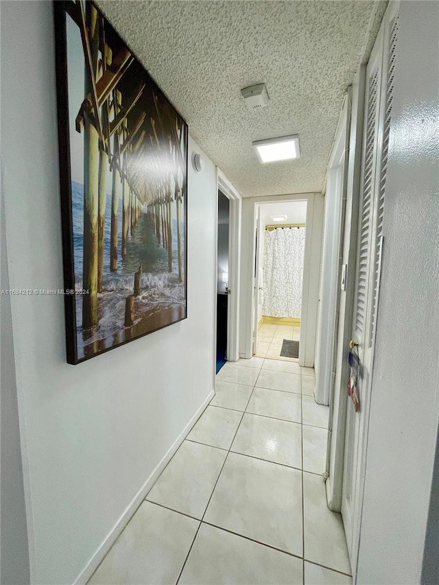 hall with a textured ceiling and light tile patterned flooring