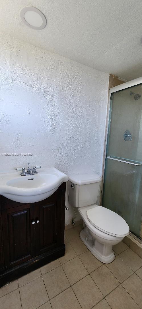 bathroom featuring a textured ceiling, toilet, tile patterned floors, walk in shower, and vanity