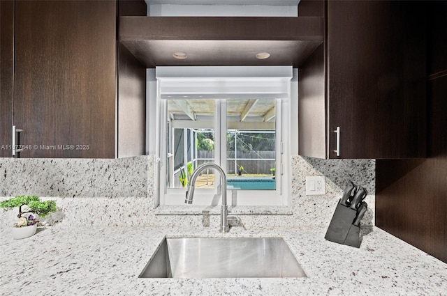 kitchen with tasteful backsplash, light stone countertops, sink, and dark brown cabinets