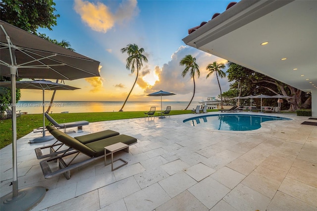 pool at dusk featuring a patio and a water view