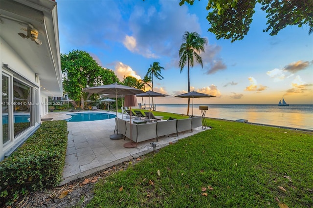 pool at dusk with a patio area, a yard, and a water view