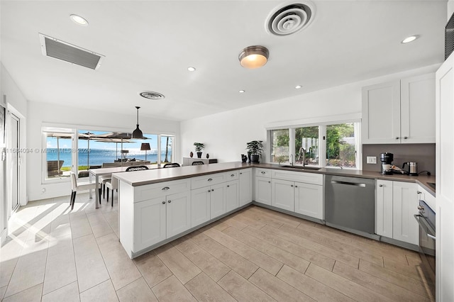 kitchen with a water view, white cabinets, stainless steel dishwasher, and hanging light fixtures