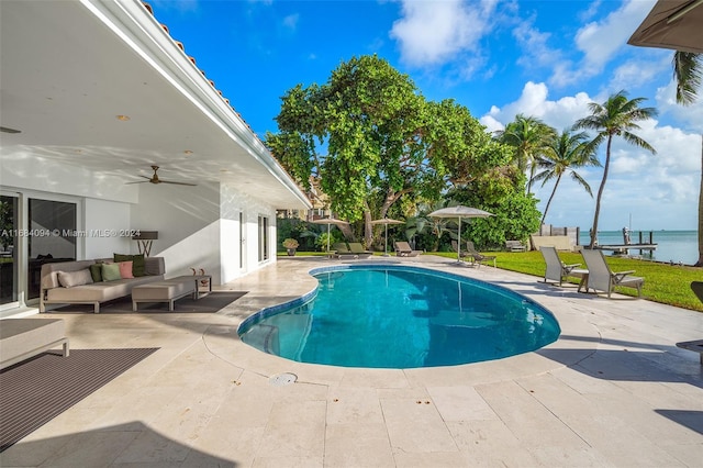 view of pool with a patio, ceiling fan, a water view, an outdoor living space, and a lawn