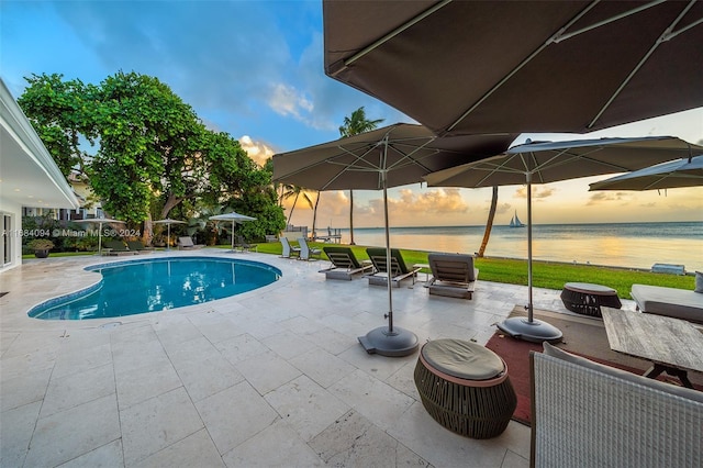 pool at dusk with a patio area and a water view