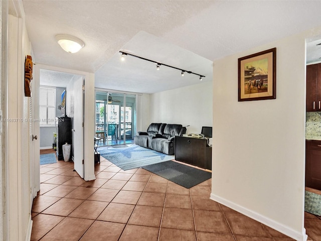 hall featuring a textured ceiling, rail lighting, and light tile patterned floors