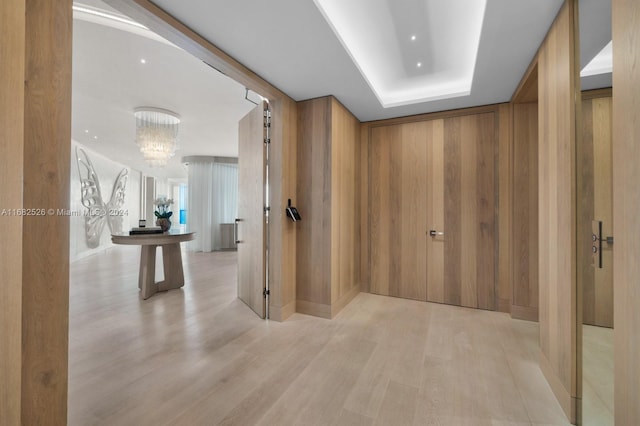 corridor featuring light hardwood / wood-style flooring, wooden walls, and a notable chandelier