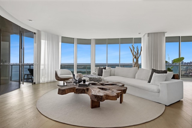 living room with floor to ceiling windows, a water view, and light wood-type flooring