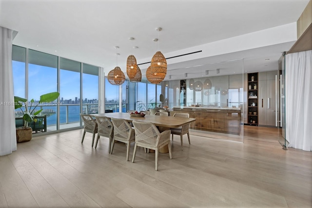 dining area with a water view, light hardwood / wood-style flooring, and a wall of windows