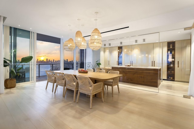 dining area featuring an inviting chandelier, a water view, light hardwood / wood-style floors, and a wall of windows