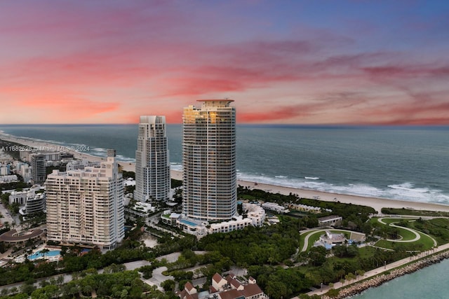 aerial view at dusk featuring a water view and a beach view