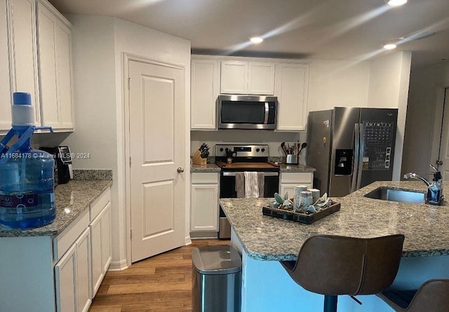 kitchen featuring sink, light stone countertops, white cabinets, light wood-type flooring, and appliances with stainless steel finishes