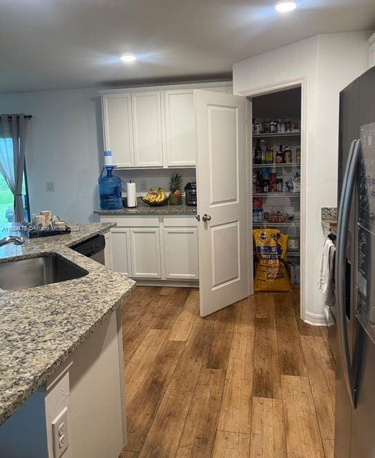 kitchen with sink, white cabinetry, stainless steel appliances, light stone counters, and light hardwood / wood-style flooring