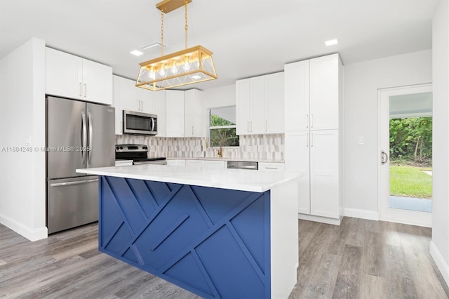 kitchen with pendant lighting, white cabinets, a kitchen island, stainless steel appliances, and tasteful backsplash