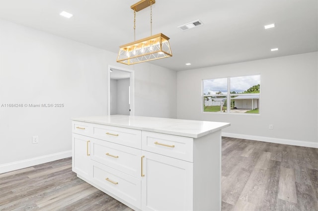 kitchen with light stone countertops, white cabinetry, light hardwood / wood-style flooring, and hanging light fixtures