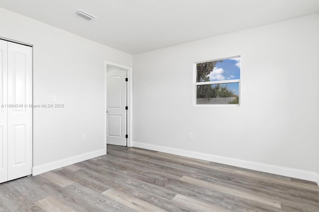 unfurnished bedroom with baseboards, a closet, visible vents, and wood finished floors