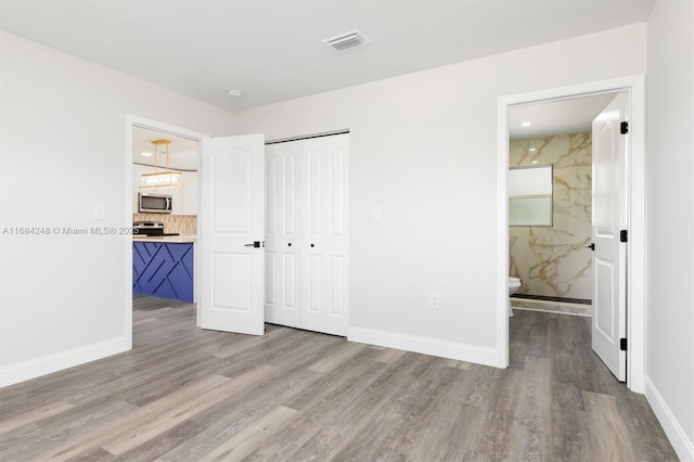 unfurnished bedroom featuring hardwood / wood-style floors, a closet, and ensuite bath