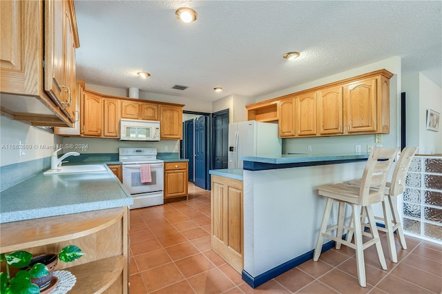 kitchen with white appliances, sink, a textured ceiling, tile patterned floors, and a breakfast bar area