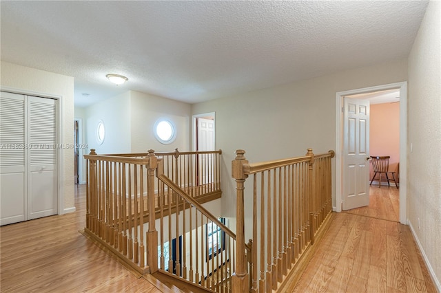 corridor with a textured ceiling and light hardwood / wood-style flooring