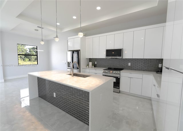 kitchen with a kitchen island with sink, stainless steel appliances, sink, pendant lighting, and white cabinetry