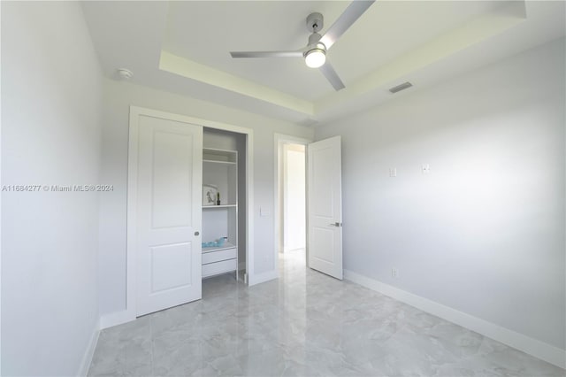 unfurnished bedroom featuring a closet, ceiling fan, and a tray ceiling