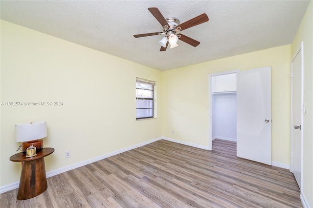 unfurnished bedroom with a closet, a walk in closet, light wood-type flooring, a textured ceiling, and ceiling fan