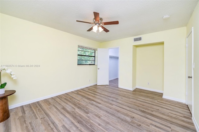 unfurnished bedroom featuring a closet, a walk in closet, light wood-type flooring, and ceiling fan