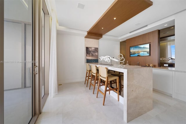 kitchen featuring kitchen peninsula, white cabinetry, and a kitchen bar