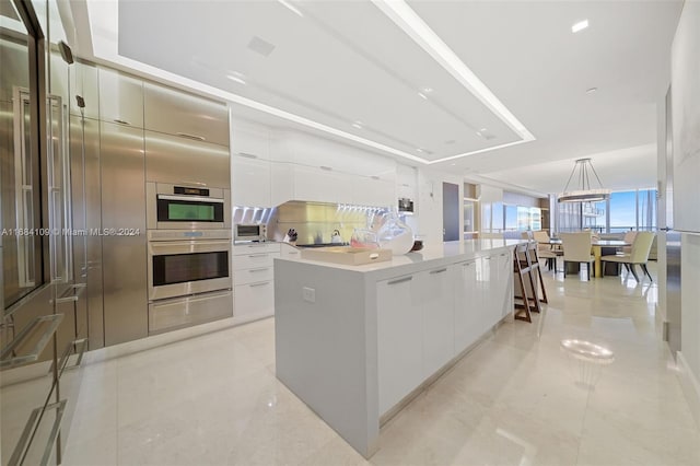 kitchen with white cabinets, backsplash, a spacious island, pendant lighting, and double oven