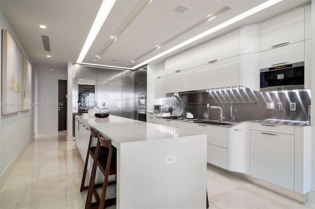 kitchen featuring a large island, white cabinets, light tile patterned floors, backsplash, and a breakfast bar area