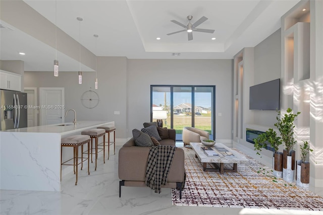 living room featuring a raised ceiling, ceiling fan, and sink