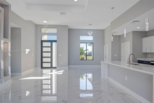 kitchen featuring white cabinetry, sink, a raised ceiling, a notable chandelier, and pendant lighting