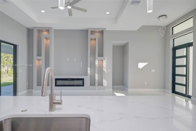 interior space with ceiling fan with notable chandelier, a tray ceiling, light stone counters, and sink