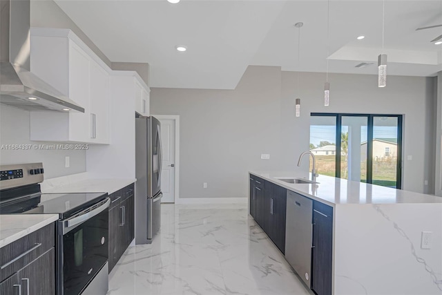 kitchen featuring white cabinets, wall chimney range hood, sink, appliances with stainless steel finishes, and decorative light fixtures