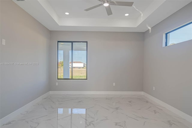 empty room with ceiling fan and a tray ceiling