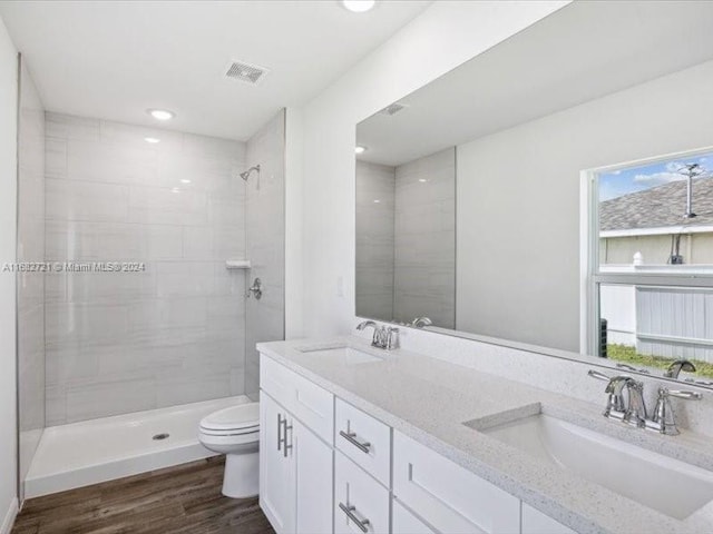 bathroom with toilet, hardwood / wood-style flooring, vanity, and tiled shower