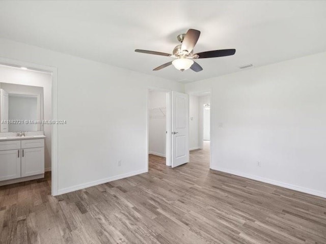 unfurnished bedroom featuring sink, a spacious closet, a closet, ceiling fan, and light hardwood / wood-style flooring