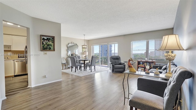 living area featuring a textured ceiling, light wood-type flooring, and baseboards