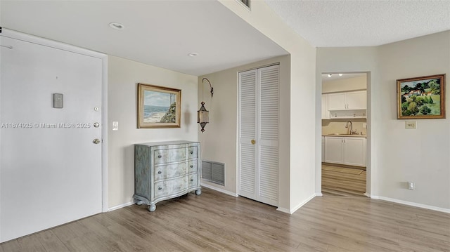 foyer entrance with light wood-type flooring, visible vents, a textured ceiling, and baseboards