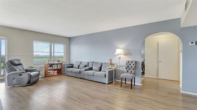 living area with arched walkways, light wood finished floors, a textured ceiling, and baseboards